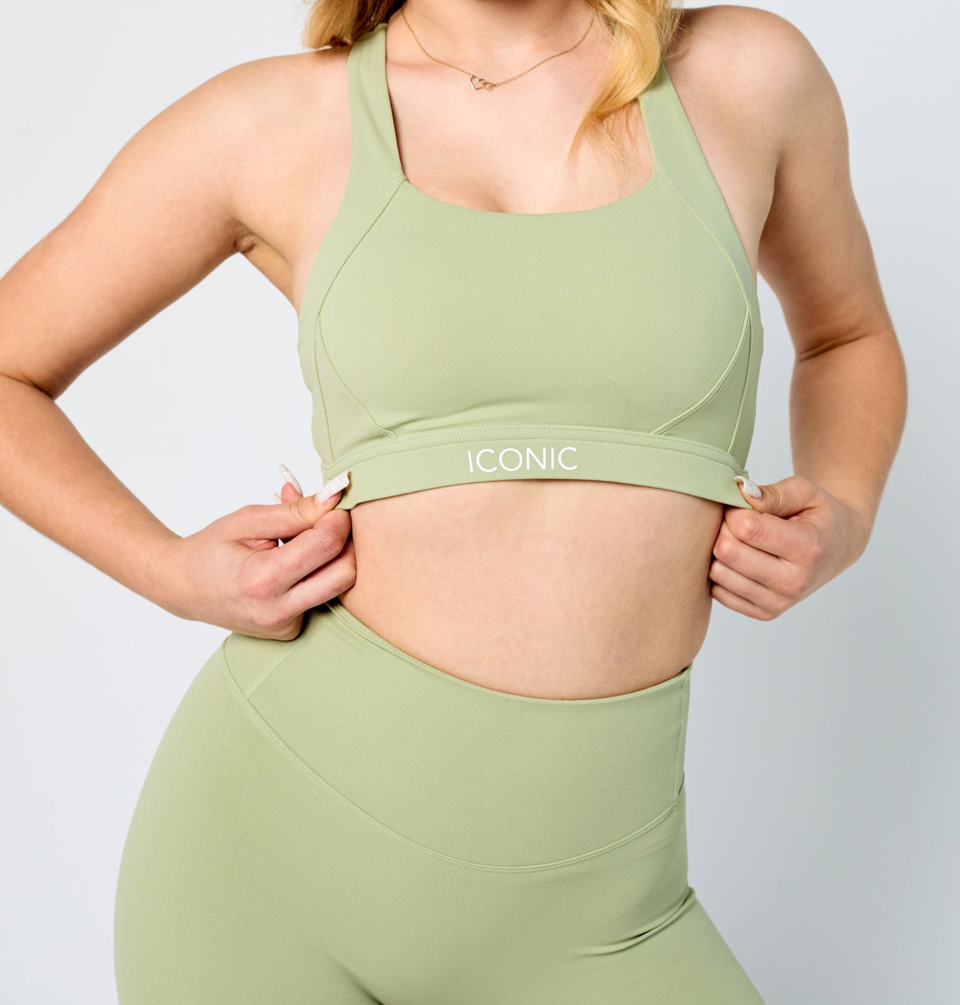 Person wearing a green sports bra and leggings with 'Iconic' branding on a light gray background