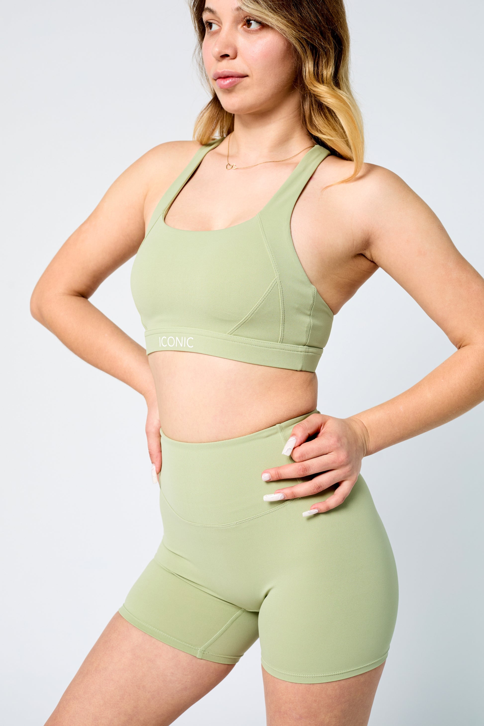 Woman wearing a green sports bra and shorts set on a light gray background