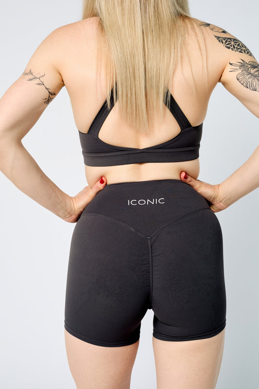 Person wearing black sports bra and shorts with 'Iconic' branding on a light gray background