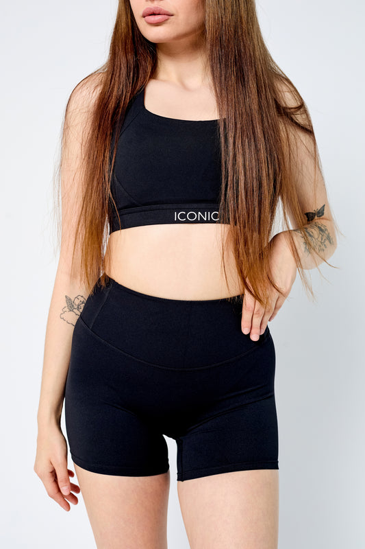 Woman wearing a black sports bra and shorts with 'Iconic' branding on a white background
